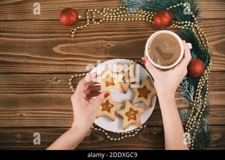 Main féminine tenant une tasse de chocolat chaud ou de chocolat avec Sur une table en bois avec biscuits au pain d'épice et décoration de Noël Banque D'Images