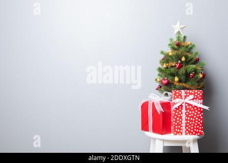 Boîtes-cadeaux rouges avec rubans blancs et petites décorations Arbre de Noël sur la table, sur fond de mur gris Banque D'Images