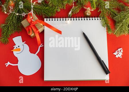 Décorations de vacances et un cahier vierge pour noter la liste des buts et des souhaits pour la nouvelle année. Noël sur fond rouge. Concept de planification Banque D'Images