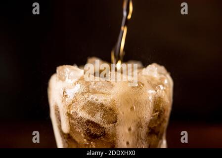 Gros plan de la boisson fraîche gazeuse gazeuse au cola versé dans le verre avec une bulle de mousse débordements sur le dessus Banque D'Images