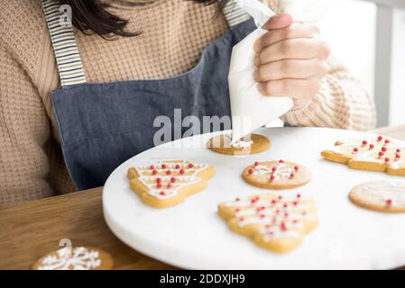 Jeune femme décorant des biscuits de Noël maison de pain d'épice avec glaçage royal sucre sur plateau blanc Banque D'Images