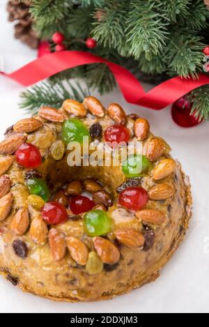 Gâteau de Noël rond vitrifié et coloré recouvert d'amandes et cerises de glace sur plaque blanche avec aiguilles de pin vert et décorations de ruban Banque D'Images
