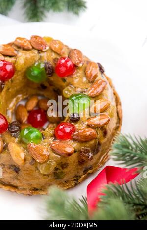 Gâteau de Noël rond vitrifié et coloré recouvert d'amandes et cerises de glace sur plaque blanche avec aiguilles de pin vert et ruban décoratif rouge Banque D'Images