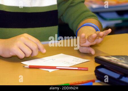 étudiant à l'école élémentaire calculant avec les doigts et écrivant dessus un morceau de papier Banque D'Images