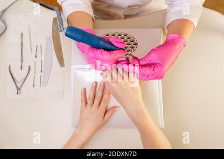 Médecine, cosmétologie et manucure. Femme maître de manucure, en gants roses faisant client de manucure dans le salon. Couper la couche supérieure. La vue depuis l' Banque D'Images