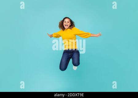 Joyeuse femme afro-américaine dans un t-shirt jaune coloré et bleu jean jumping isolé sur fond bleu Banque D'Images