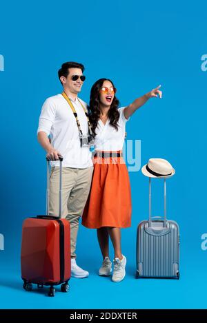 Couple touristique interracial souriant avec bagages appréciant leur été escapade de vacances ensemble dans un décor de studio bleu Banque D'Images