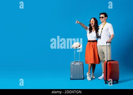 Couple touristique interracial souriant avec bagages appréciant leur été escapade de vacances ensemble dans un décor de studio bleu Banque D'Images