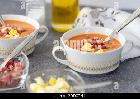 Un gros plan de la délicieuse soupe salmorejo servie avec du jambon un bol blanc avec une cuillère sur une table Banque D'Images