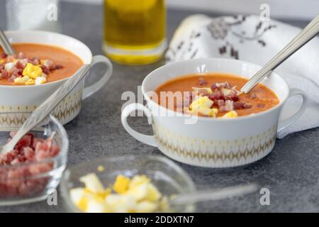 Un gros plan de la délicieuse soupe salmorejo servie avec du jambon un bol blanc avec une cuillère sur une table Banque D'Images