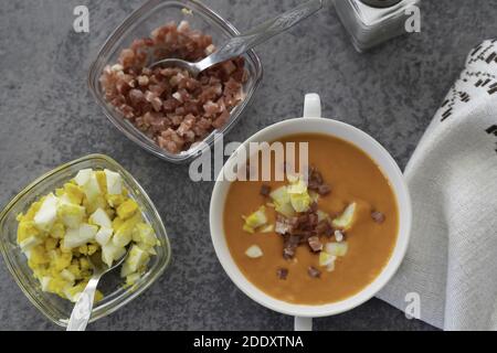 Un gros plan de la délicieuse soupe salmorejo servie avec du jambon un bol blanc avec une cuillère sur une table Banque D'Images