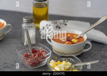 Un gros plan de la délicieuse soupe salmorejo servie avec du jambon un bol blanc avec une cuillère sur une table Banque D'Images