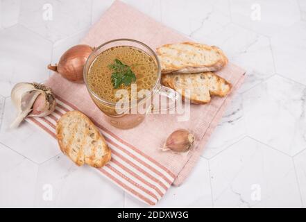 Bouillon de viande copieux dans une tasse de verre sur une serviette sur fond clair. Banque D'Images