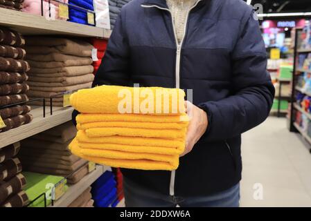 Un homme tient une pile de serviettes dans un magasin. Articles d'hygiène, serviettes de bain jaunes douces et moelleuses dans le supermarché Banque D'Images