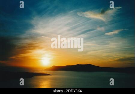 Vue depuis la ville de Thira (Thera) du soleil se coucher sur la caldeira et la mer Égée, avec les îles Thirasia et Nea Kameni silhouetted ; Santorini, Grèce Banque D'Images