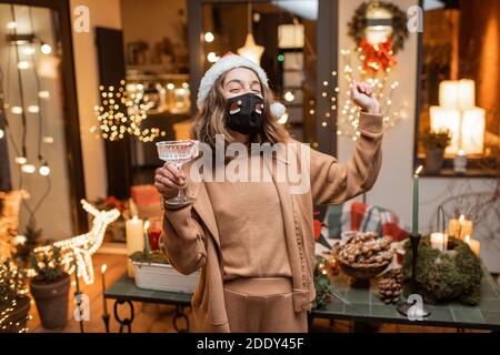 Jeune femme heureuse en masque facial célébrant seul les vacances du nouvel an à la maison. Concept de quarantaine et d'auto-isolement pendant l'épidémie en vacances Banque D'Images