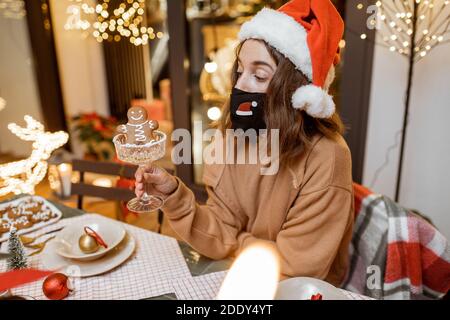 Jeune femme en masque facial célébrant seul les vacances du nouvel an à la maison. Concept de quarantaine et d'auto-isolement pendant l'épidémie en vacances Banque D'Images