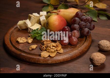 Assiette de fruits, raisins, noix sur une assiette en bois foncé et table en bois. Assortiment d'en-cas au vin : sélection de fromages, raisins, poires et noix sur un Banque D'Images