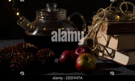 Théière en verre, vieux livres, pins et pommes. Guirlande lumineuse. Image de nuit. Ambiance de Noël. Banque D'Images