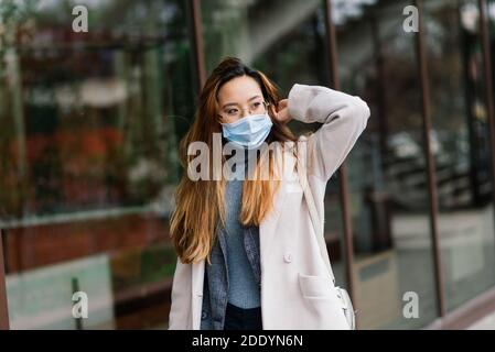 Jeune femme asiatique avec masque chirurgical de protection du visage. Elle se rend entre la maison et le lieu de travail en ville Banque D'Images