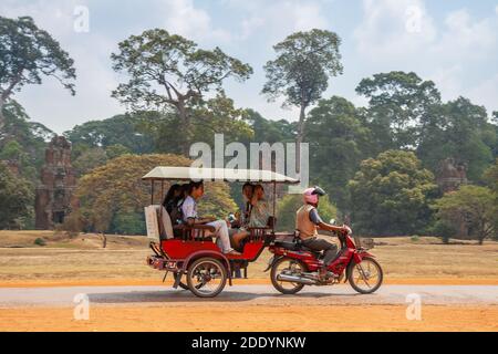 SIEM REAP, CAMBODGE - FÉVRIER 2013 : tuk-tuk en pousse-pousse avec des touristes asiatiques sur la route du temple d'Angkor Thom, Cambodge Banque D'Images