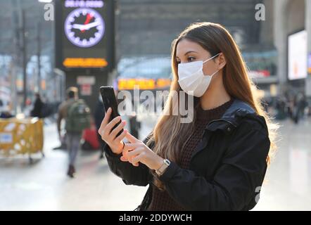 Femme d'affaires portant un masque de protection achetant un billet en ligne avec un smartphone à la gare Banque D'Images