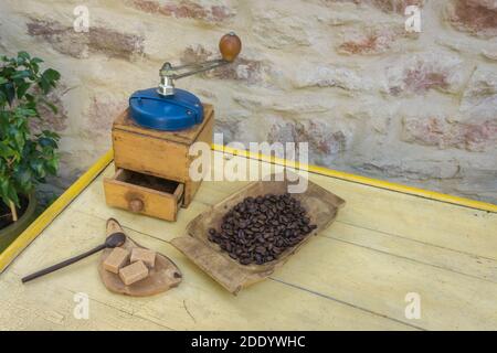Moulin à café manuel vintage et grains de café sur une ancienne table en bois. Arrière-plan - mur de pierre. Banque D'Images