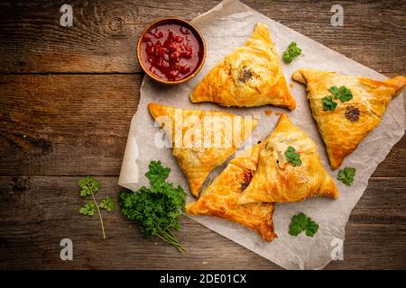 Samsa ou samosas avec viande et légumes avec sauce tomate sur fond de bois. Cuisine asiatique traditionnelle. Vue de dessus. Banque D'Images