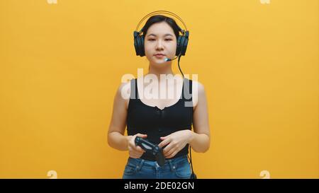 Jeune femme asiatique concentrée avec casque et manette joyeuse jouant aux jeux vidéo. Isolé sur fond jaune. Photo de haute qualité Banque D'Images
