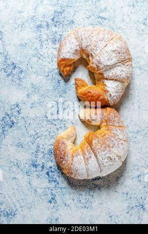 Deux croissants frais avec sucre glace sur un bleu arrière-plan avec texture Banque D'Images