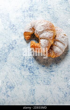 Deux croissants frais avec sucre glace sur un bleu arrière-plan avec texture Banque D'Images