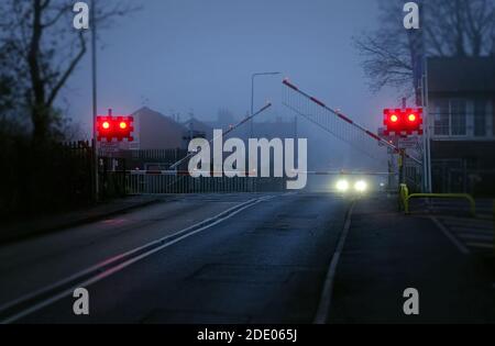 Une route atmosphérique brumeuse à Bingham, dans le Notinghamshire, où les barrières descendent sur un passage à niveau. Banque D'Images