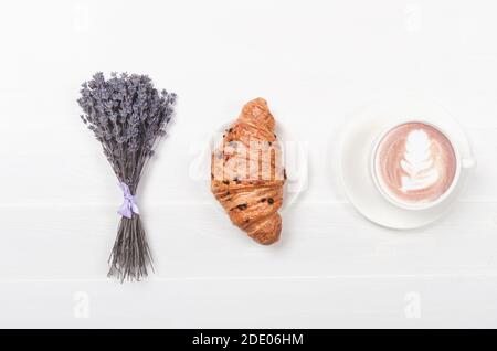 Café au lait avec croissant sur une table en bois blanc et fleur de lavande violette séchée. Vue sur le dessus Banque D'Images