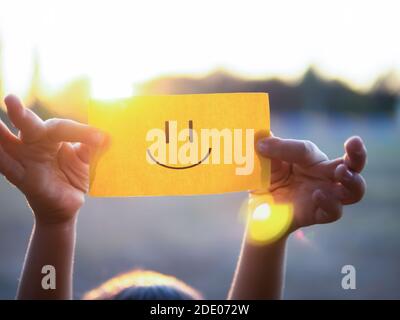 Un enfant tient un papier avec un visage positif sur lui, mettant le soleil Banque D'Images