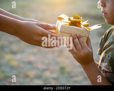 Un garçon donne à un enfant une boîte cadeau avec du ruban doré, mettant le soleil. Concept de vacances Banque D'Images