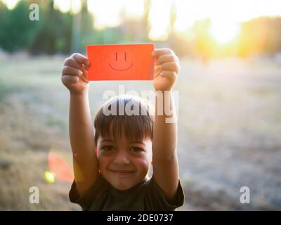 Un enfant tient un papier avec un visage positif sur lui, mettant le soleil Banque D'Images