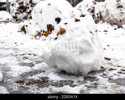 boule de neige de la première neige avec feuilles mortes collées pelouse gelée dans le parc de la ville le jour d'automne froid Banque D'Images
