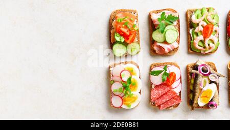 Ensemble de différents sandwichs avec viande, légumes et fruits de mer. Assortiment de sandwichs ouverts sur fond de pierre claire avec espace de texte libre. Vue de dessus, plate Banque D'Images