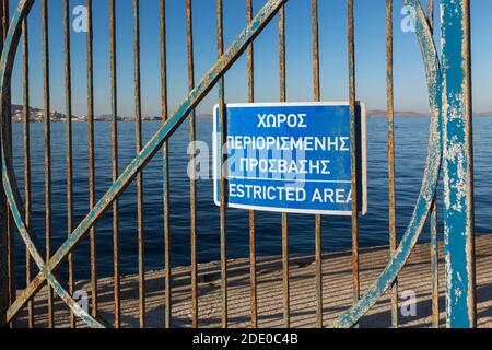 Gros plan du panneau d'avertissement de zone réglementée en grec et en anglais affiché sur la porte en fer rouillé bleu, nouveau port de Mykonos, île de Mykonos, Grèce Banque D'Images