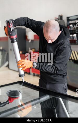 Vitrier appliquant du joint en caoutchouc sur le pare-brise dans le garage, gros plan. Photo de haute qualité Banque D'Images