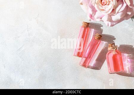 Eau de rose parfumée ou huile essentielle en bouteille de verre et fleur de rose sur fond clair. Mise au point sélective, espace de copie Banque D'Images