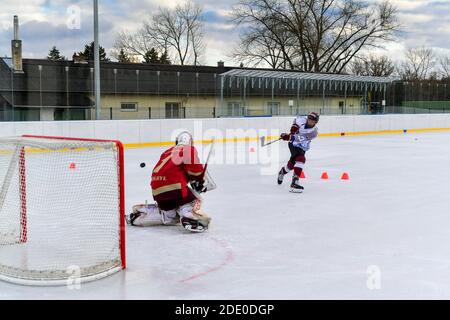 un joueur de hockey de jeunesse prend des coups de feu sur le gardien de but pendant le hockey sur glace en plein air formation Banque D'Images