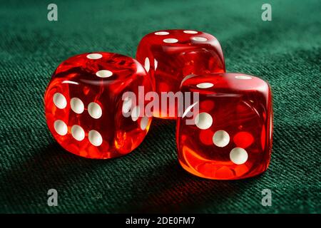 Trois dés transparents en acrylique rouge pour les jeux. Jeux de dés translucides sur une surface en velours vert foncé, gros plan, grande profondeur de champ. Banque D'Images