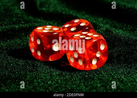 Trois dés transparents en acrylique rouge pour les jeux. Jeux de dés translucides sur une surface en velours vert foncé, gros plan, grande profondeur de champ. Banque D'Images