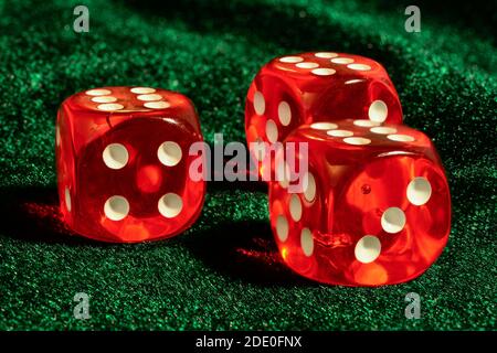 Trois dés transparents en acrylique rouge pour les jeux. Jeux de dés translucides sur une surface en velours vert foncé, gros plan, grande profondeur de champ. Banque D'Images