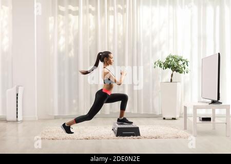 Coupe longue d'un pas d'entraînement de jeune femme aérobie devant le téléviseur à la maison Banque D'Images