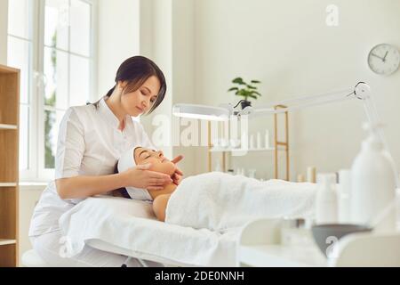 Une femme reçoit un massage du visage d'une femme masseuse professionnelle dans le bureau d'un spa moderne. Banque D'Images