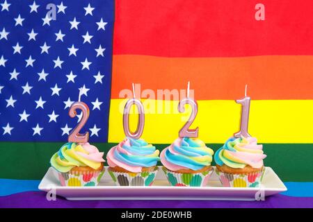 Gâteau de tasse à la vanille dépolie de couleur arc-en-ciel sur une assiette rectangulaire avec 2021 bougies du nouvel an sur le dessus en rose pastel métallisé. Gay Pride drapeau américain dans Banque D'Images