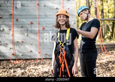 Un instructeur masculin met un équipement de protection pour l'escalade sur une jeune femme à l'extérieur du parc d'attractions Banque D'Images