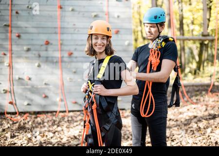 Un instructeur masculin met un équipement de protection pour l'escalade sur une jeune femme à l'extérieur du parc d'attractions Banque D'Images